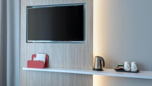 A modern room with a mounted flat-screen TV, a white shelf with a red phone, a kettle, and two white mugs. - Holiday Inn Express Oberhausen by IHG (Oberhausen)