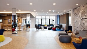 A modern lounge area with seating arrangements, a coffee station, and a large window providing natural light. - Holiday Inn Express Oberhausen by IHG (Oberhausen)