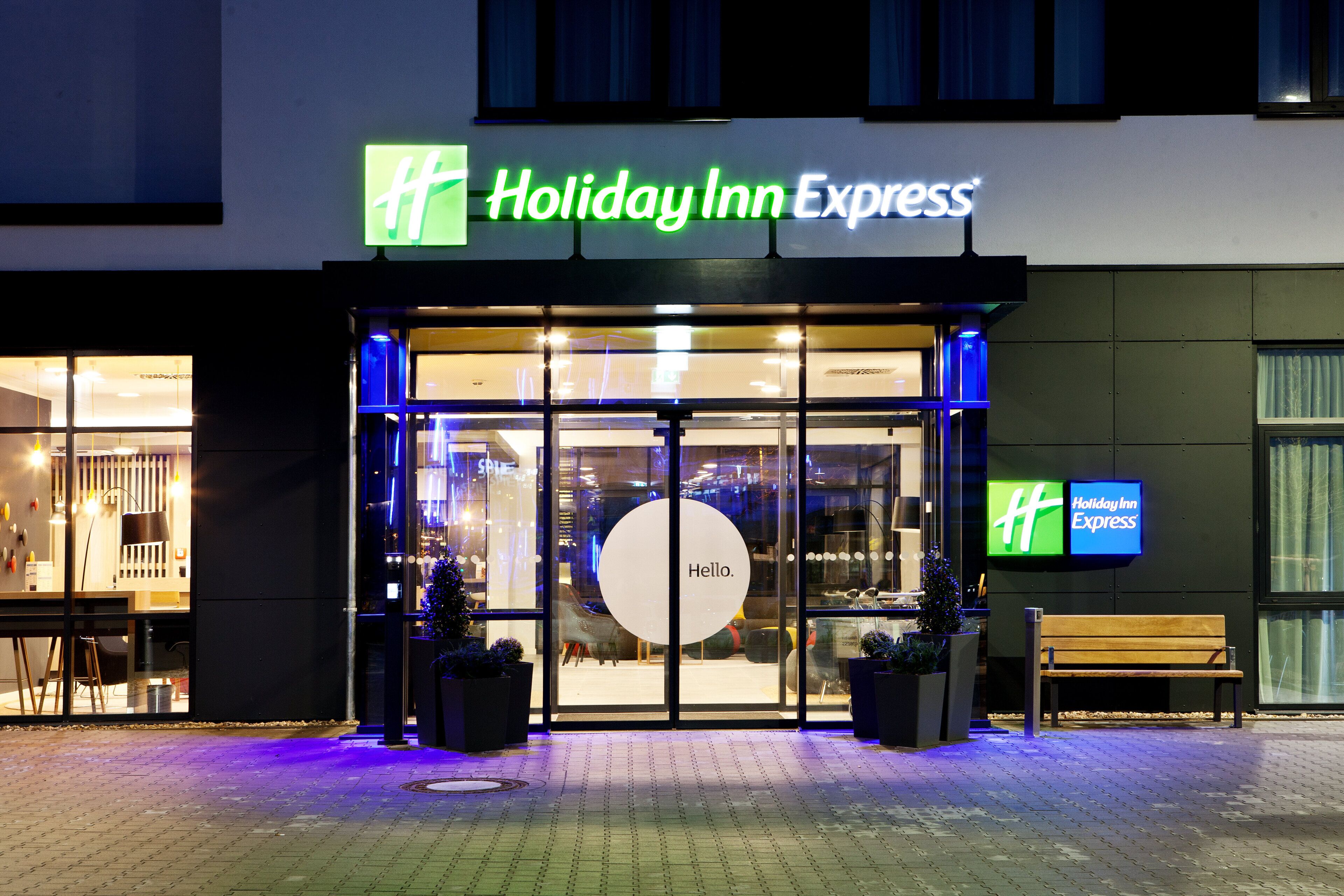 Das äußere Erscheinungsbild eines Holiday Inn Express Hotels mit einem großen Glas Eingangsbereich, einer Bank davor und einem Weihnachtsbaum.