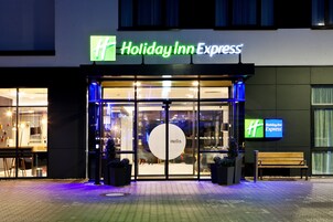 Exterior de un hotel Holiday Inn Express con una amplia entrada de vidrio, un banco afuera y un árbol de Navidad.
