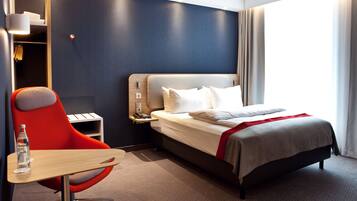 A modern hotel room with a large bed, a red chair, a small table, and a nightstand.