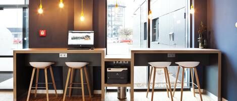 A modern bar area with wooden stools, a desktop computer, and pendant lighting.