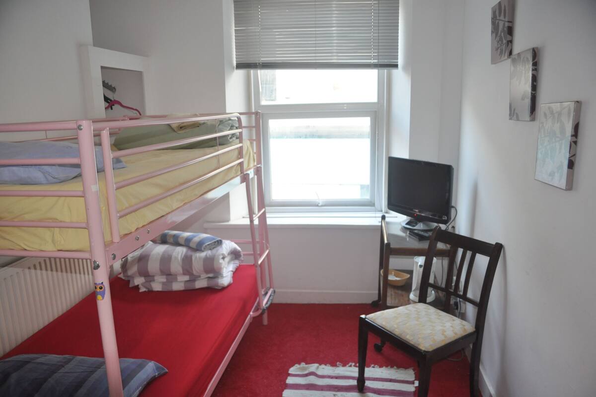 A bunk bed with a red mattress, a desk with a computer, and a chair.