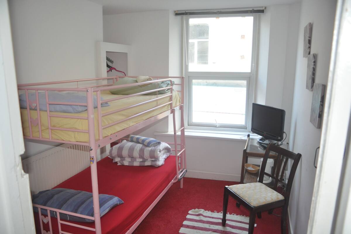 A bunk bed room with a desk and chair, a window, and a radiator.