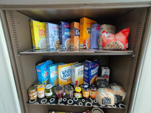A pantry with shelves stocked with various food items including cereals, jars of condiments, and bread.