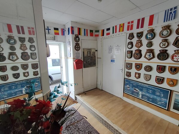 Un pasillo decorado con una colección de medallas y premios en las paredes, una planta en primer plano, y una puerta con un aviso.