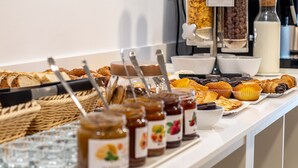 Een ontbijtbuffet met diverse gebakjes, muffins en potten jam.