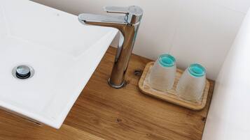 A bathroom sink with a chrome faucet, a wooden tray with two glass containers, and a white tiled wall.