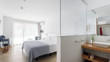 A modern hotel room with a large bed, a desk, a chair, a mirror, and a bathroom with a sink and mirror.
