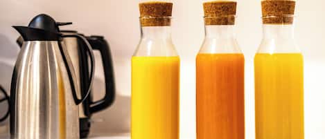 Three glass bottles with cork stoppers containing orange juice on a white countertop.