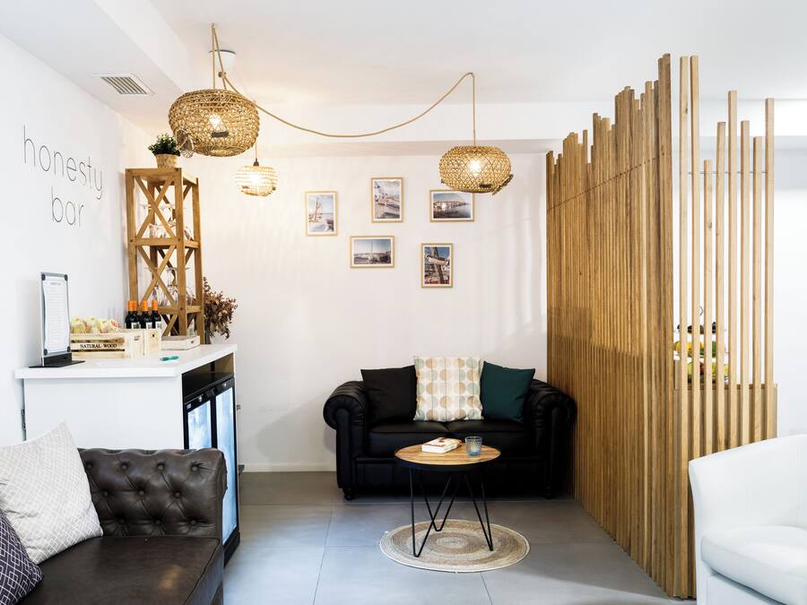 Una sala de estar moderna con un sofá negro, un sillón blanco, un separador de madera y una pequeña mesa redonda con un libro y un vaso.