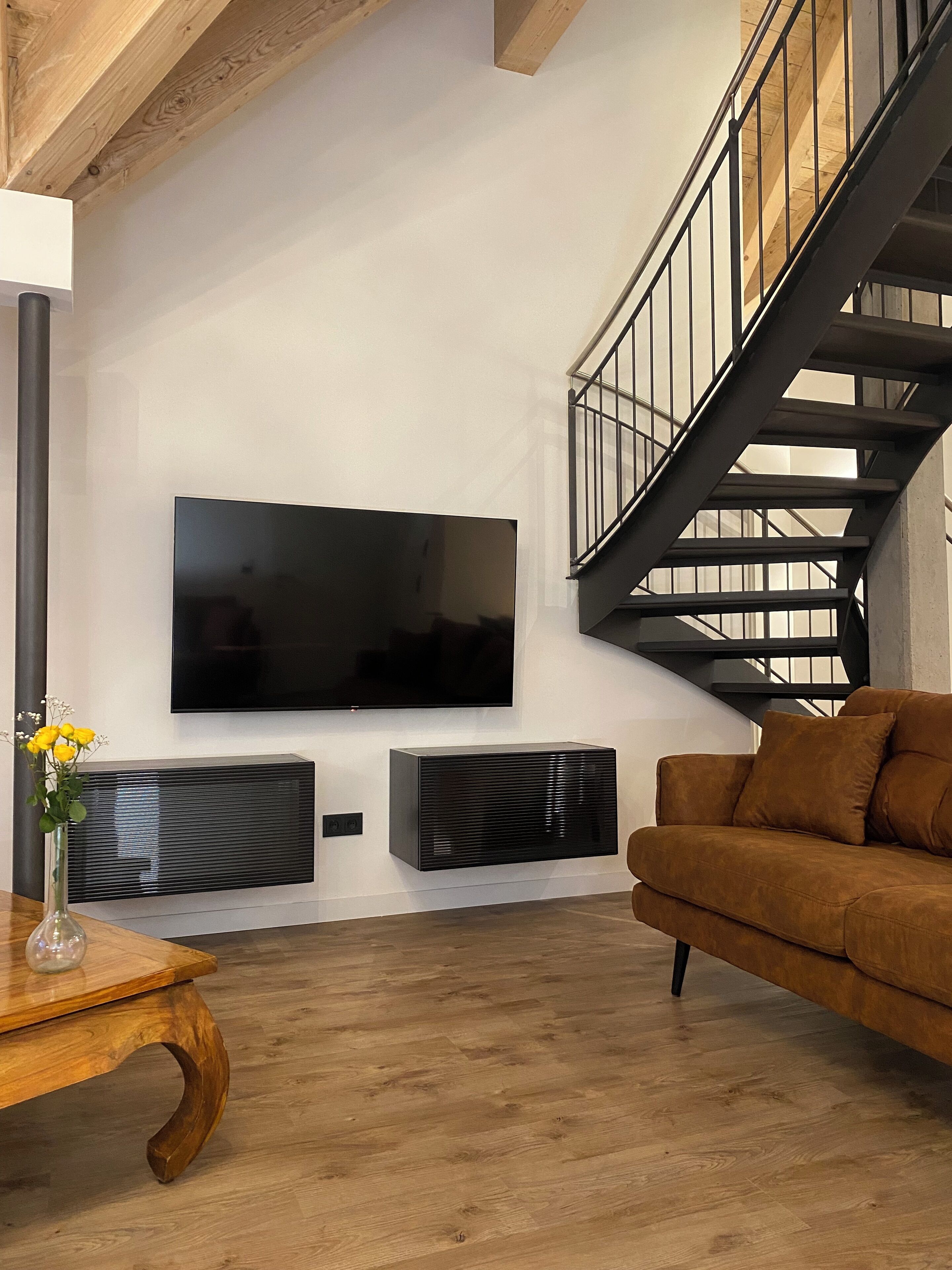 Un salon moderne avec un grand téléviseur à écran plat fixé au mur, un canapé marron et une table basse en bois.