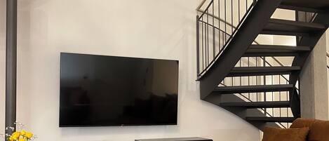 Un salon moderne avec un grand téléviseur à écran plat fixé au mur, un canapé marron et une table basse en bois.