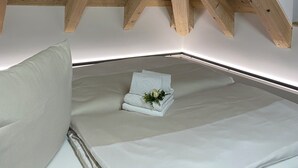 Un dormitorio con techo inclinado sostenido por vigas de madera, una cama con ropa blanca y un pequeño adorno sobre la cama.