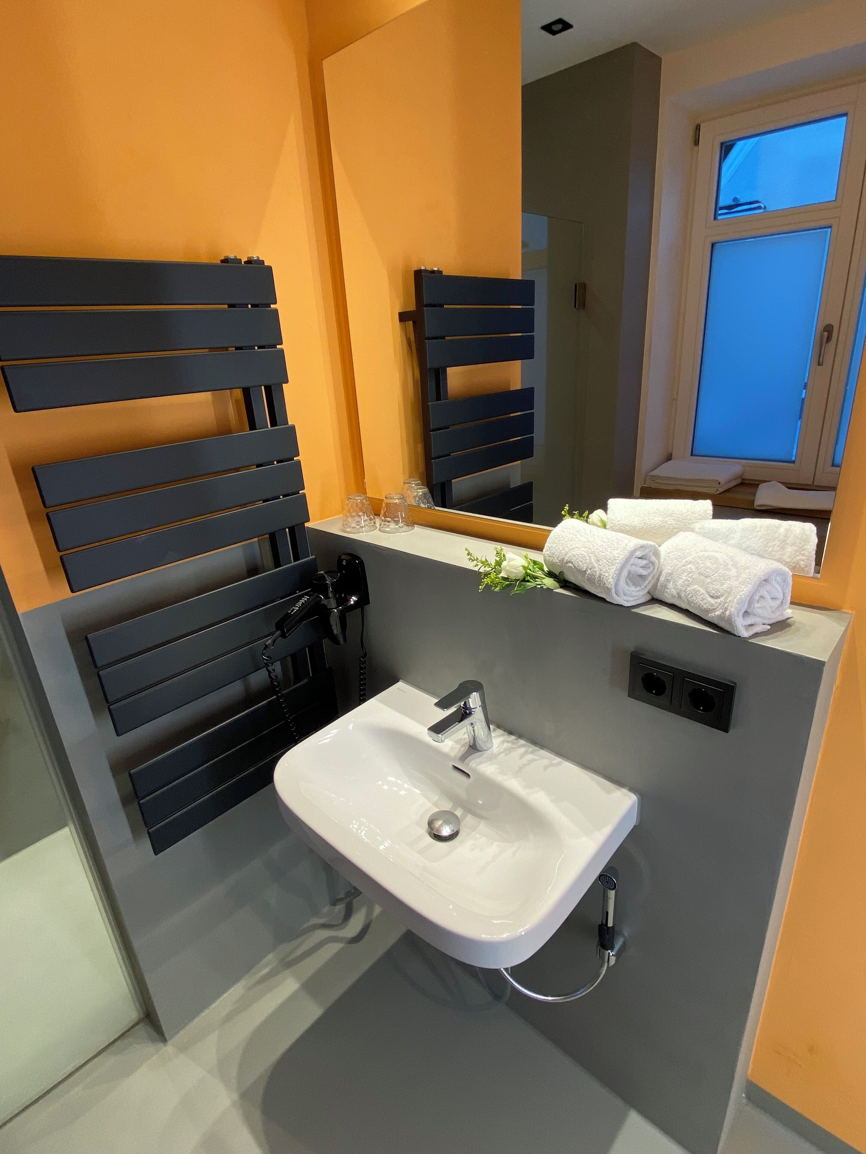 Un baño moderno con un lavabo blanco, toalleros negros y un espejo sobre el lavabo.