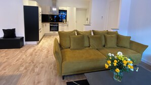 Una sala de estar moderna con un sofá, una mesita de centro con flores y una cocina al fondo.