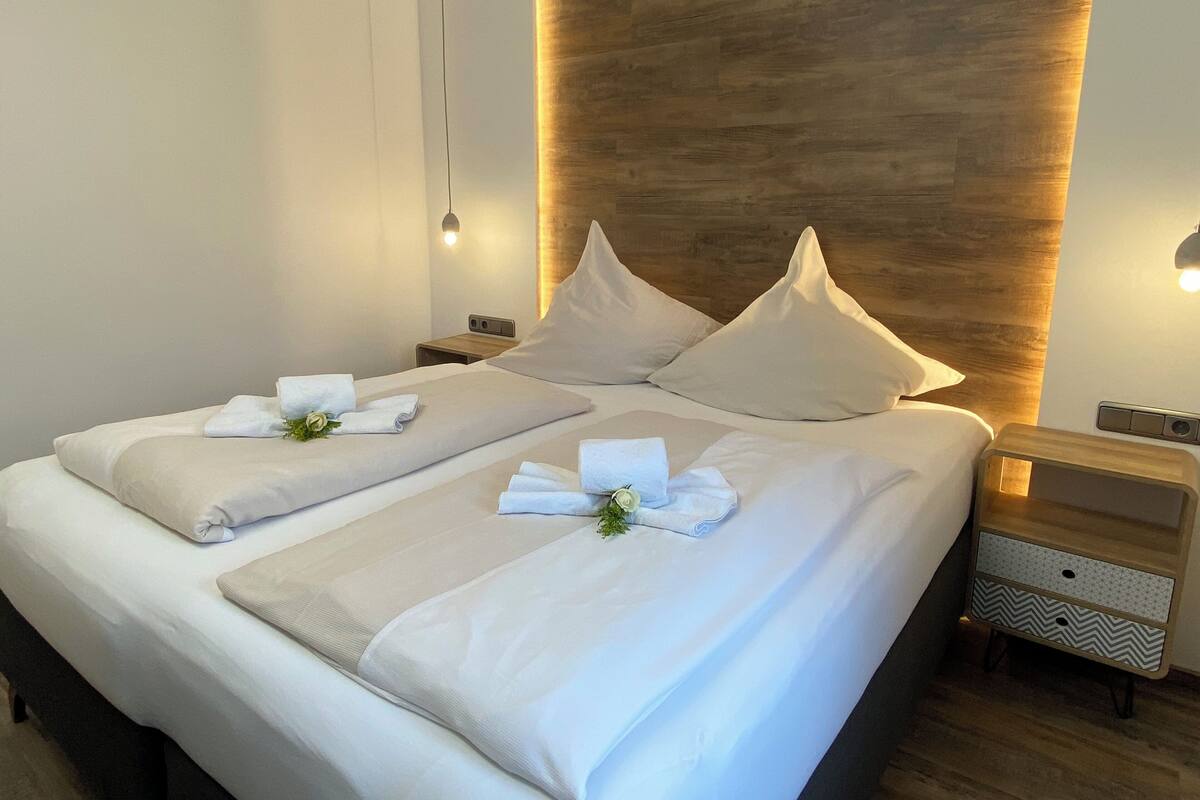 A modern hotel room with a large bed, wooden headboard, and bedside tables with lamps.