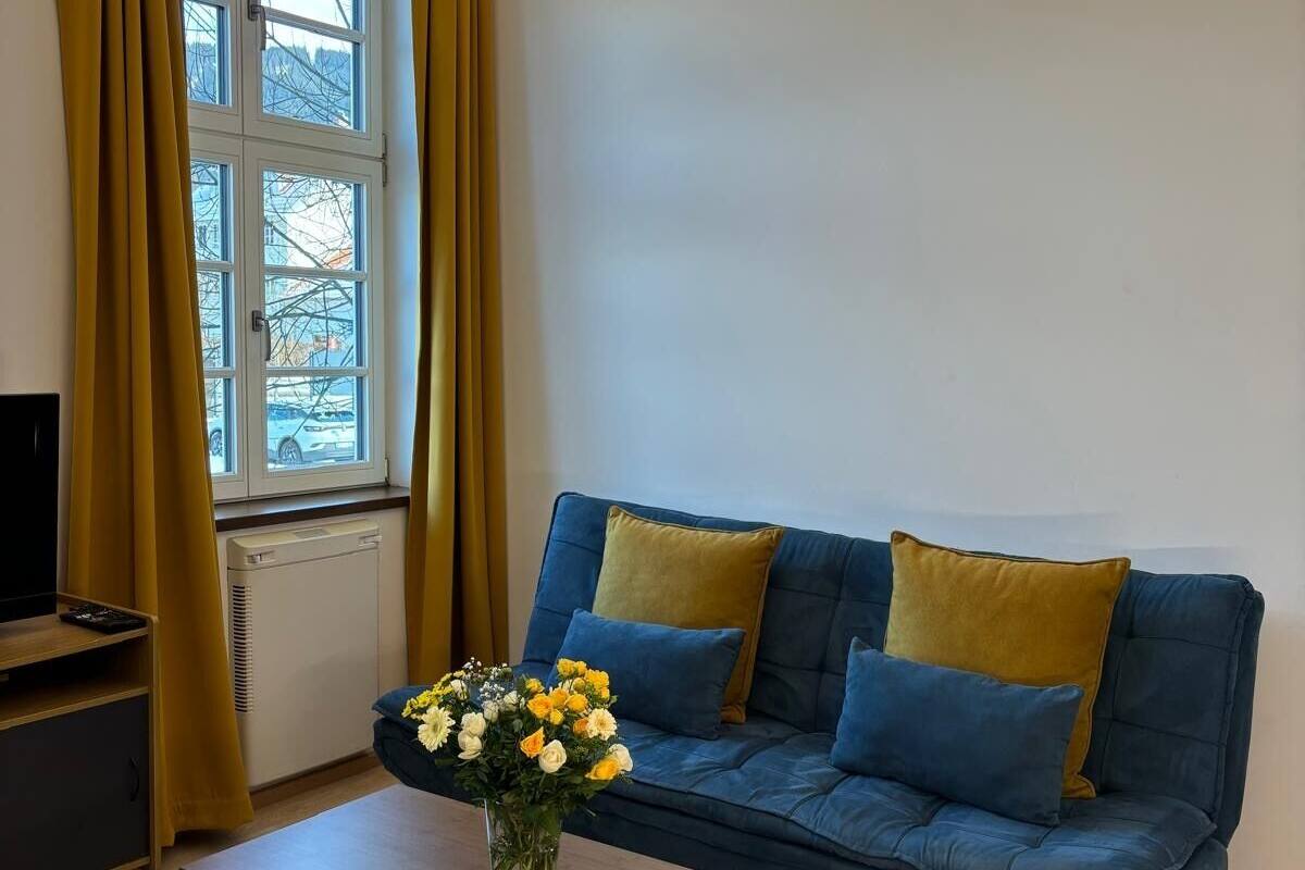 A modern living room with a blue sofa, a wooden coffee table, and a window with curtains.
