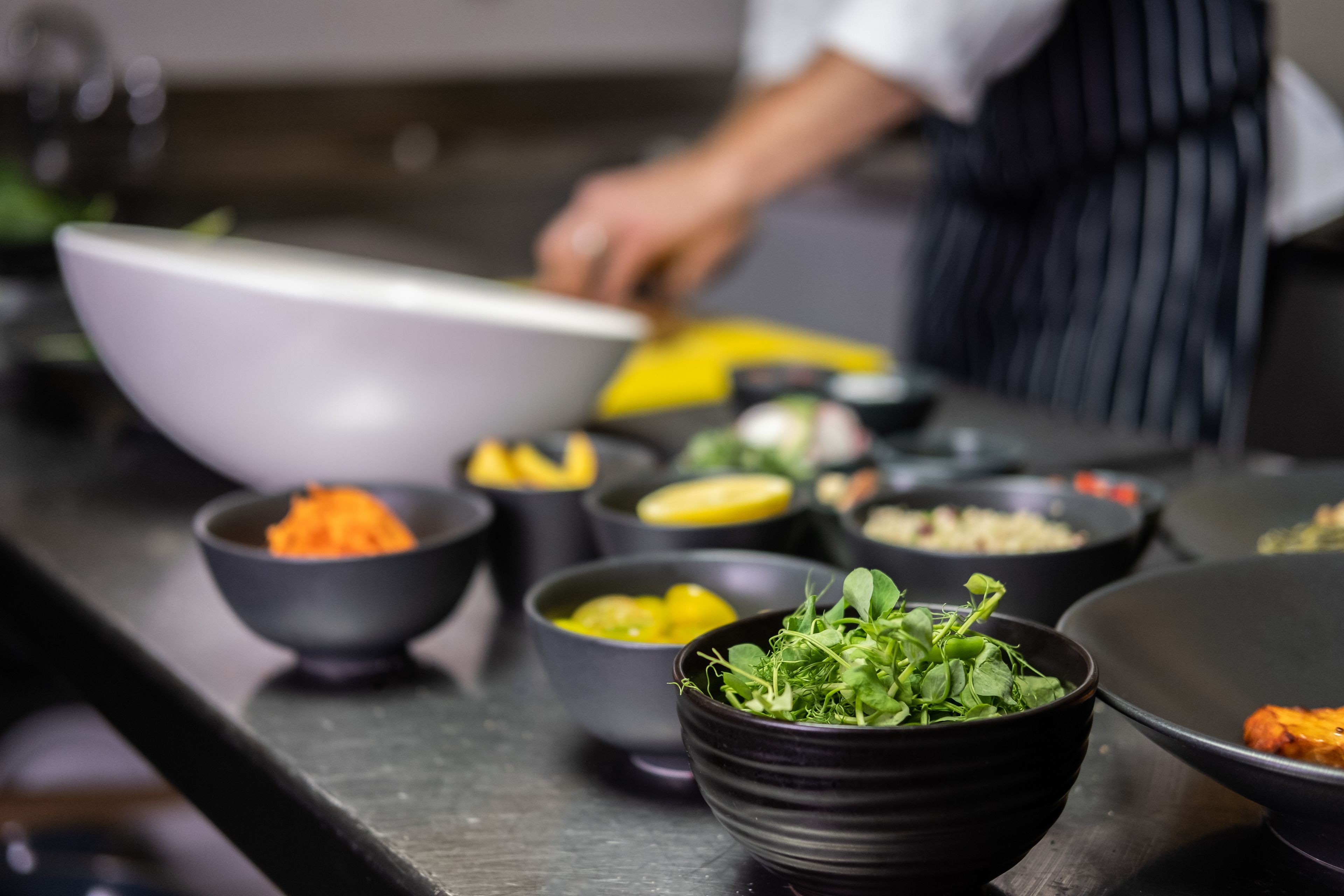 Un chef prepara comida en una cocina con varios recipientes que contienen diferentes ingredientes.