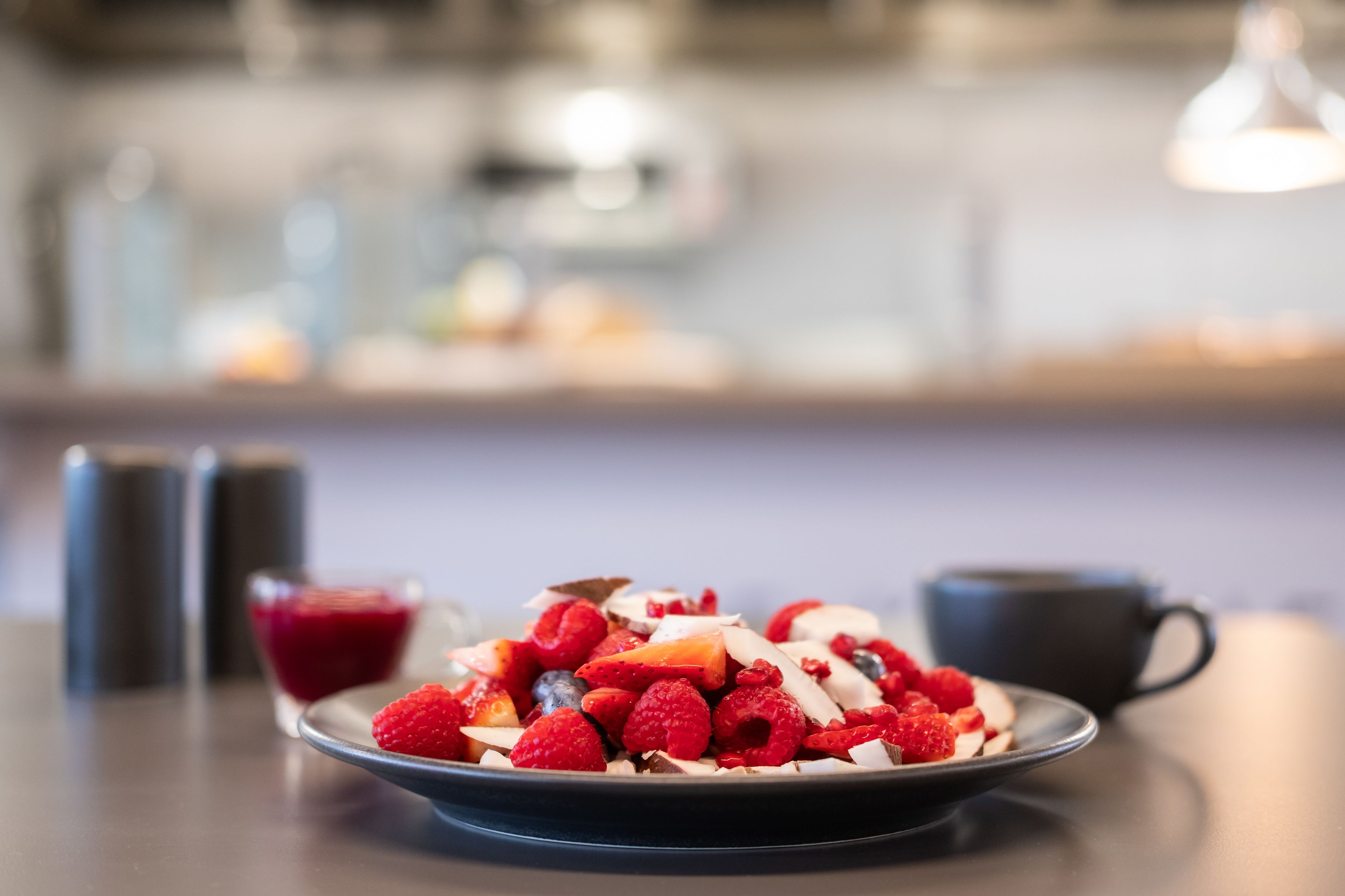 Un plato de frutos rojos y nueces sobre una mesa con fondo desenfocado.
