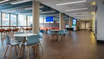 A spacious indoor area with multiple tables and chairs, large windows, and a modern ceiling design.
