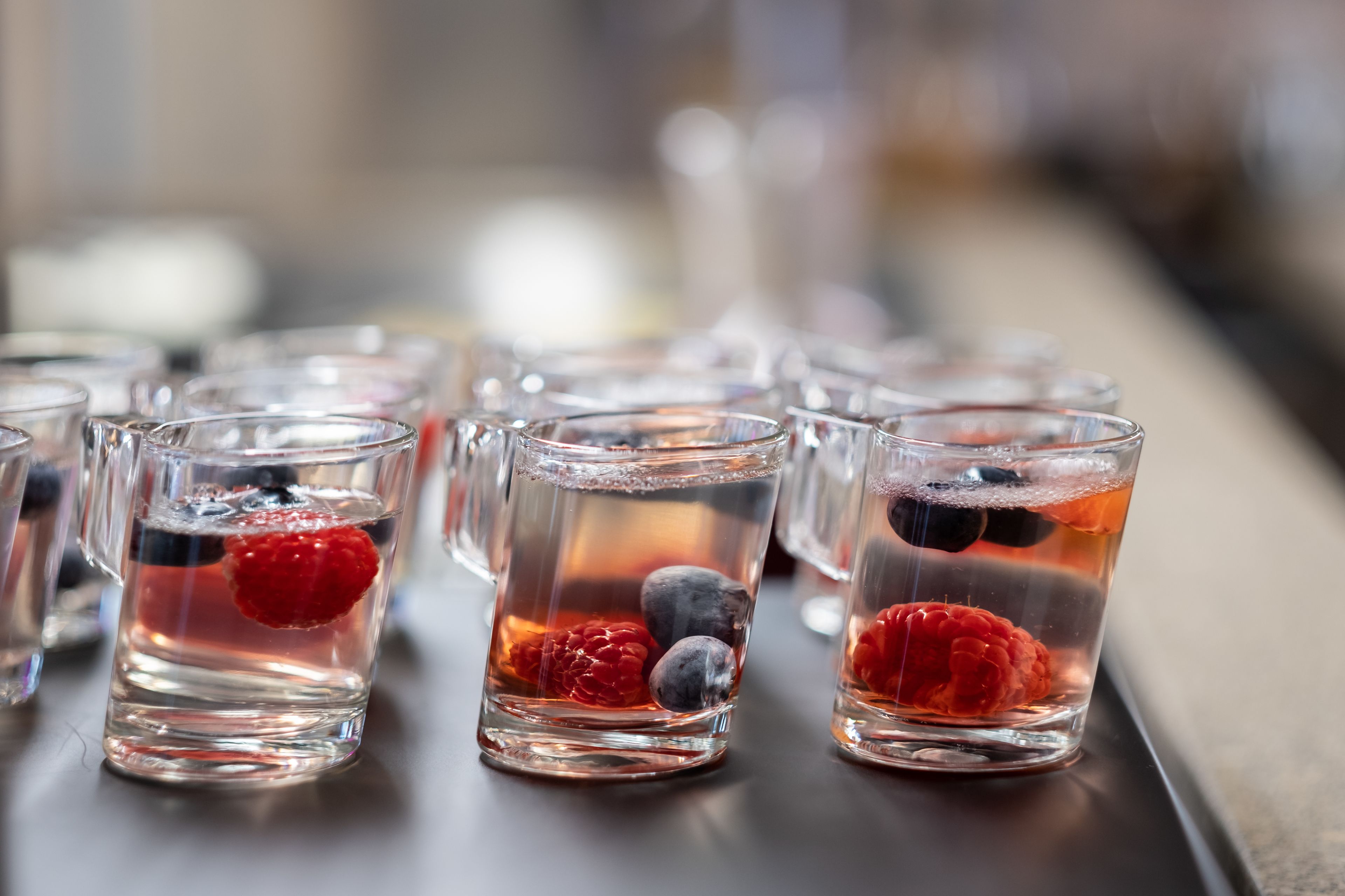 A row of clear glasses with water, raspberries, and blueberries.
