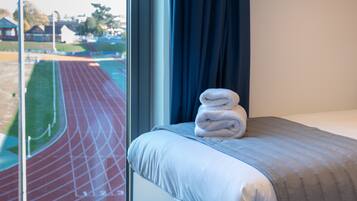 Una habitación de hotel con cama, ventana y vistas a una pista de atletismo, además de una toalla sobre la cama.