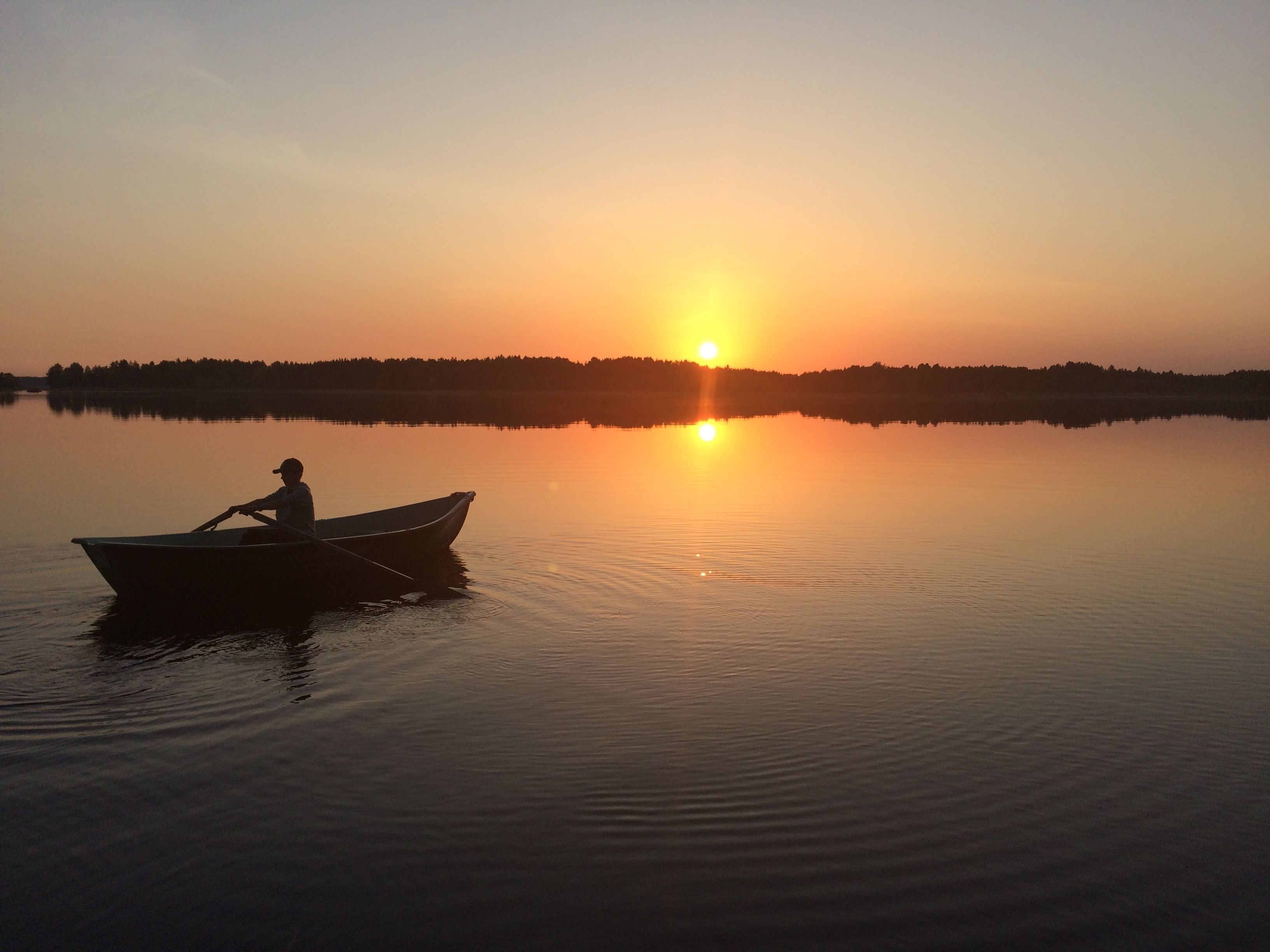 A calm lake at sunset with a boat and a person rowing.