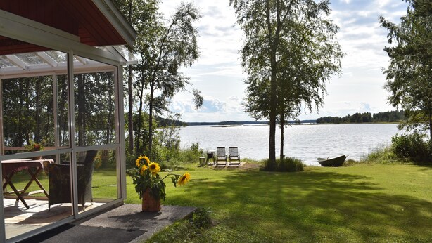 A glass-enclosed patio with a view of a lake, outdoor furniture, and a lawn. - Karjalan Helmi (Kitee)