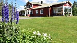 A red house with a large front porch, a garage, and a well-maintained lawn. - Karjalan Helmi (Kitee)