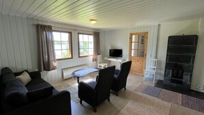 A furnished living room with a sofa, chairs, a TV, a fireplace, and a window with curtains. - Karjalan Helmi (Kitee)