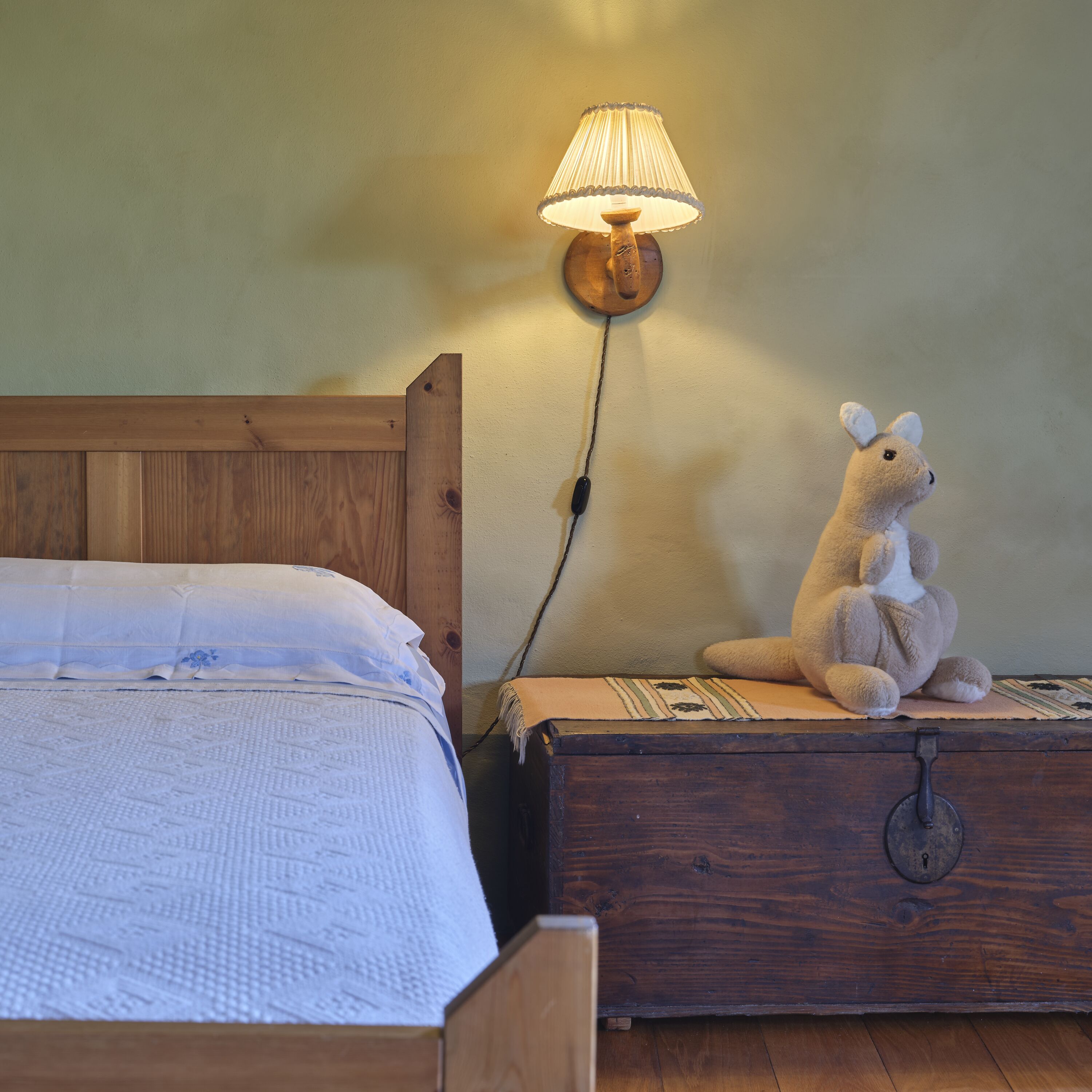 A wooden bed with a white bedspread and a lamp on a wooden nightstand beside it.