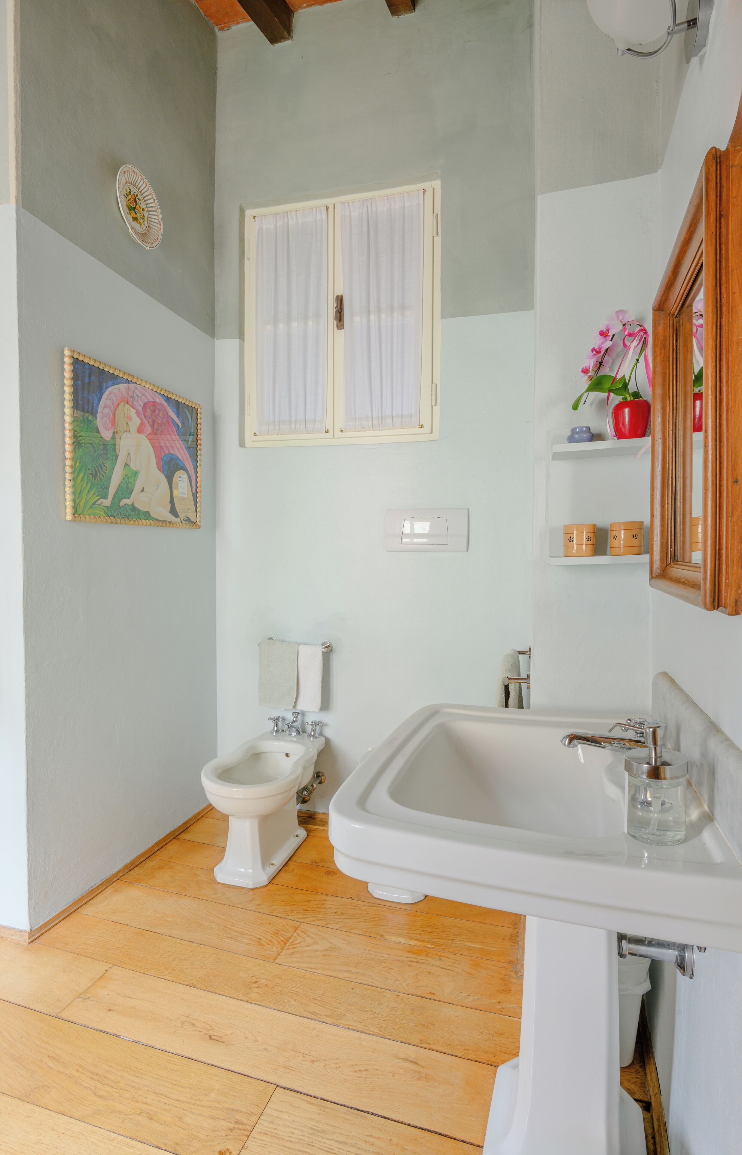 A bathroom with a white sink, a bidet, and a window with white curtains.