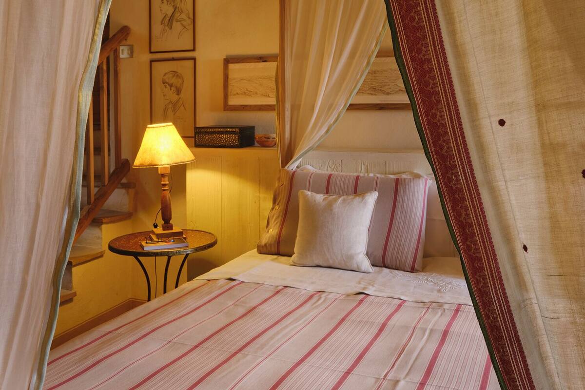 A bed with striped bedding, a bedside lamp, a small table, and a wall with framed pictures.