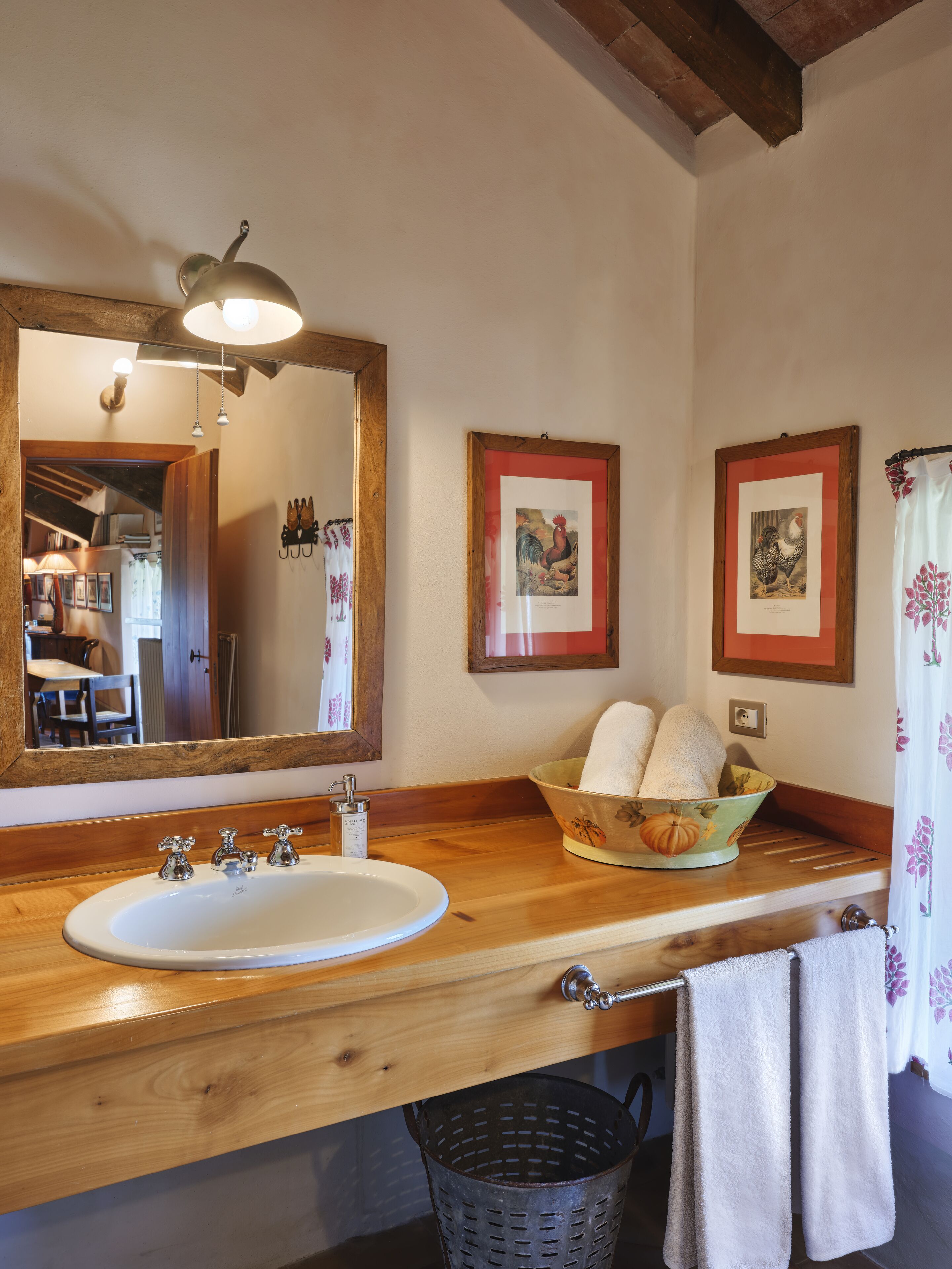 Ein Badezimmer mit einem Holzbadezimmerhocker, einem weißen Waschbecken, einem Spiegel und zwei gerahmten Bildern an der Wand.