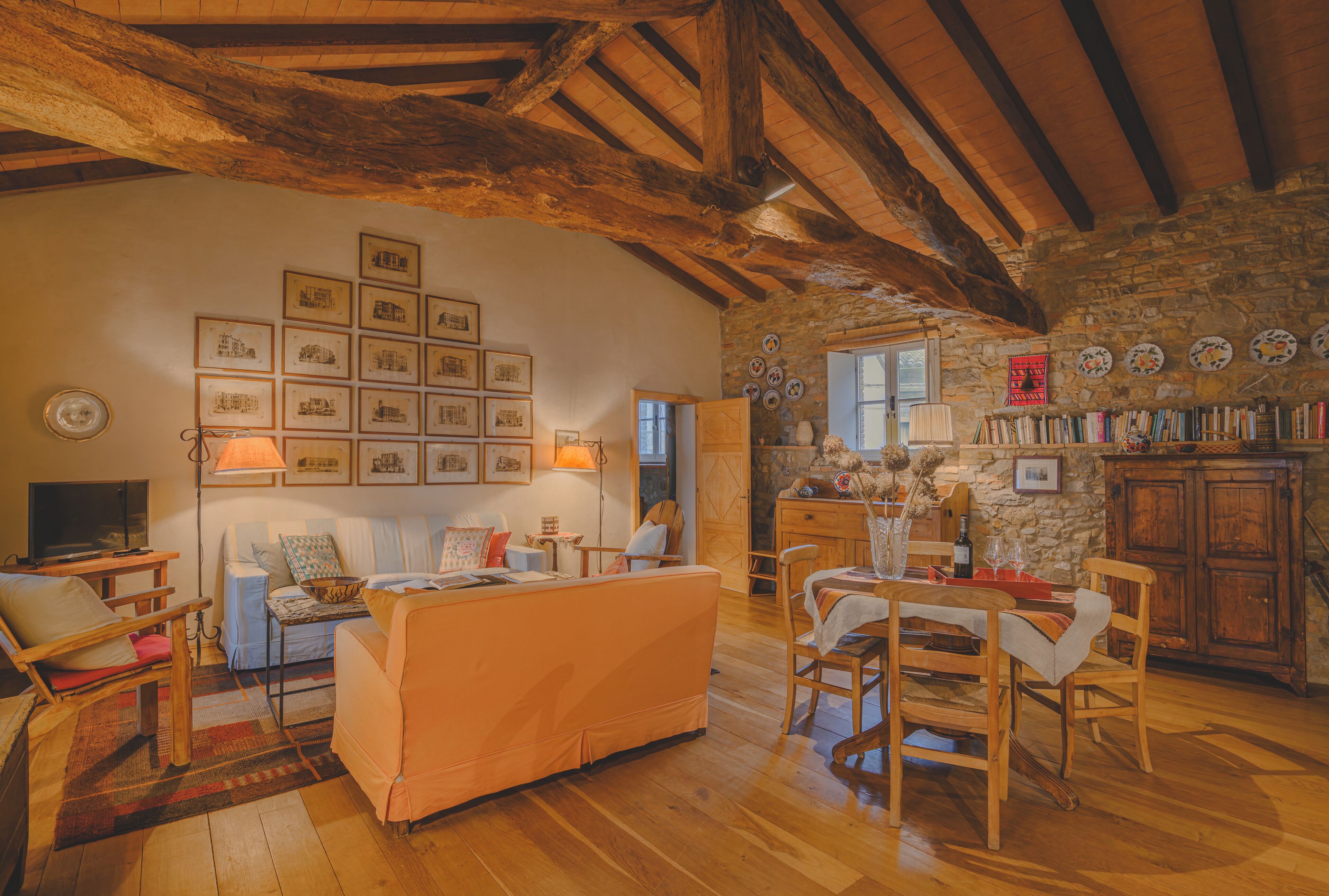 Ein gemütliches Wohnzimmer mit einer Couch, Sesseln, einem Esstisch und einer Steinwand mit gerahmten Bildern.
