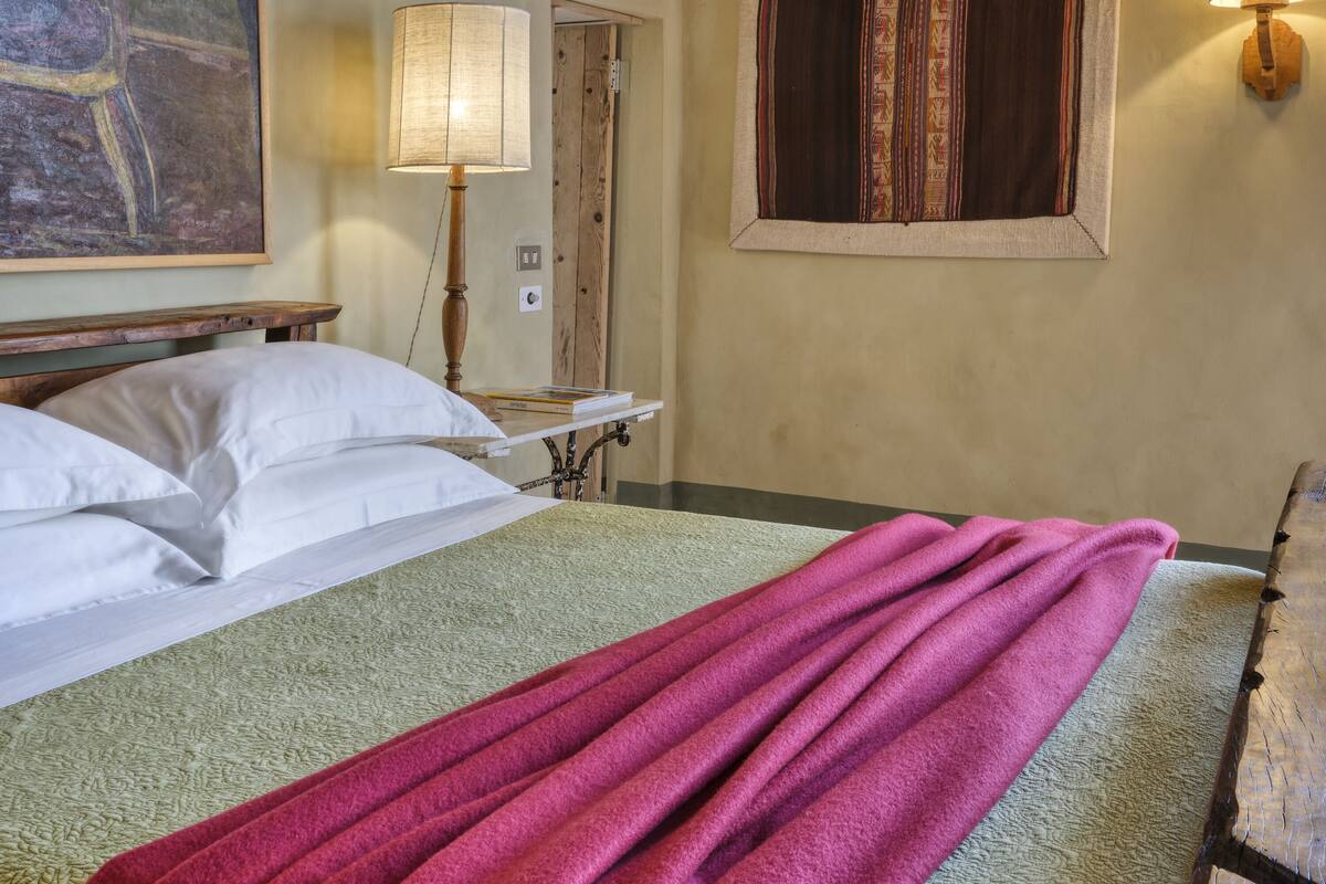 A hotel room with a bed, a window with curtains, a painting on the wall, and a lamp on the nightstand.