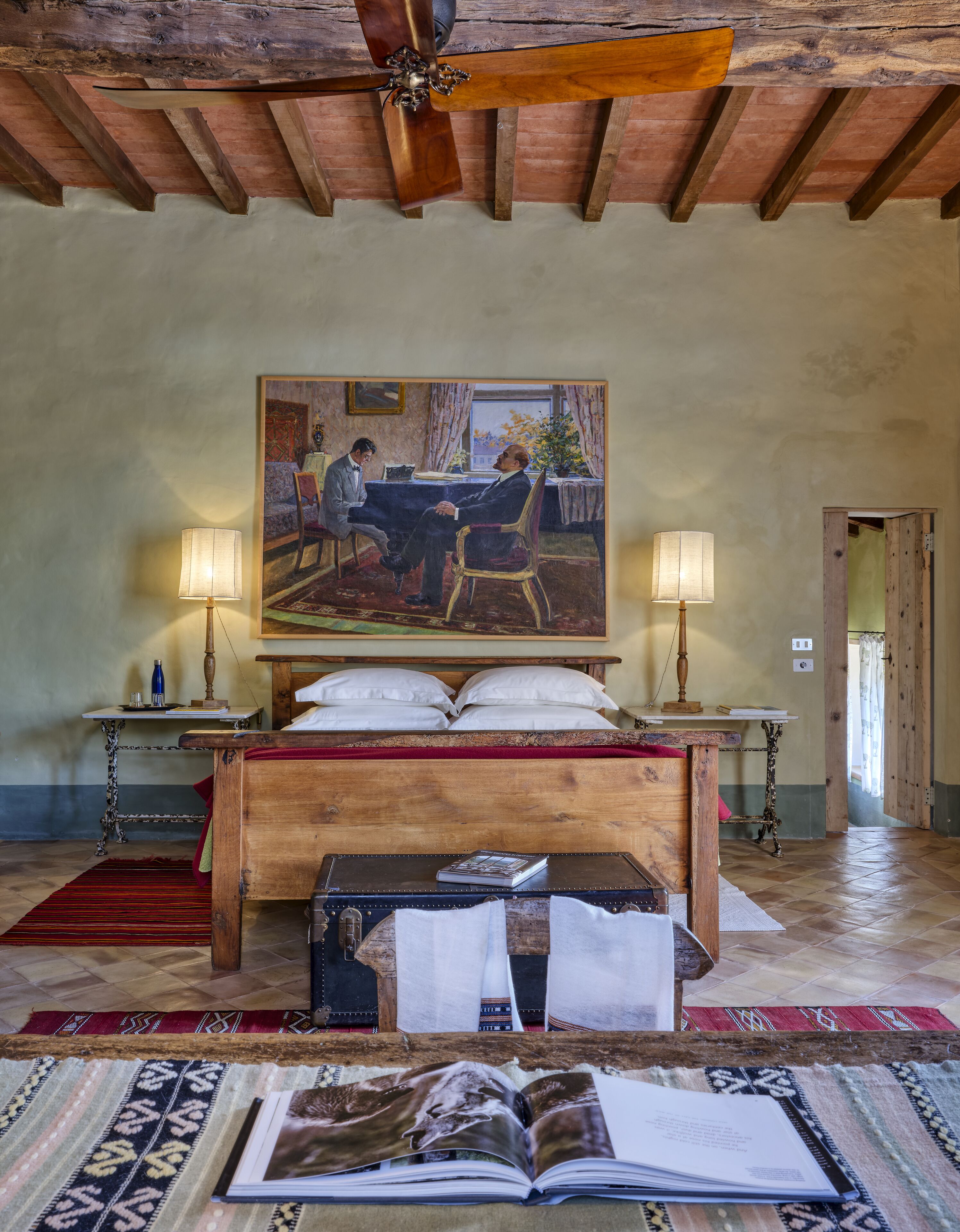 A bedroom with a wooden bed, a painting on the wall, two bedside lamps, and a large window.