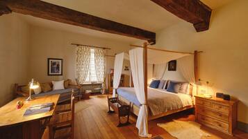 Un dormitorio con cama con dosel, un escritorio de madera, una silla, un radiador y una mesita de noche con lámpara.
