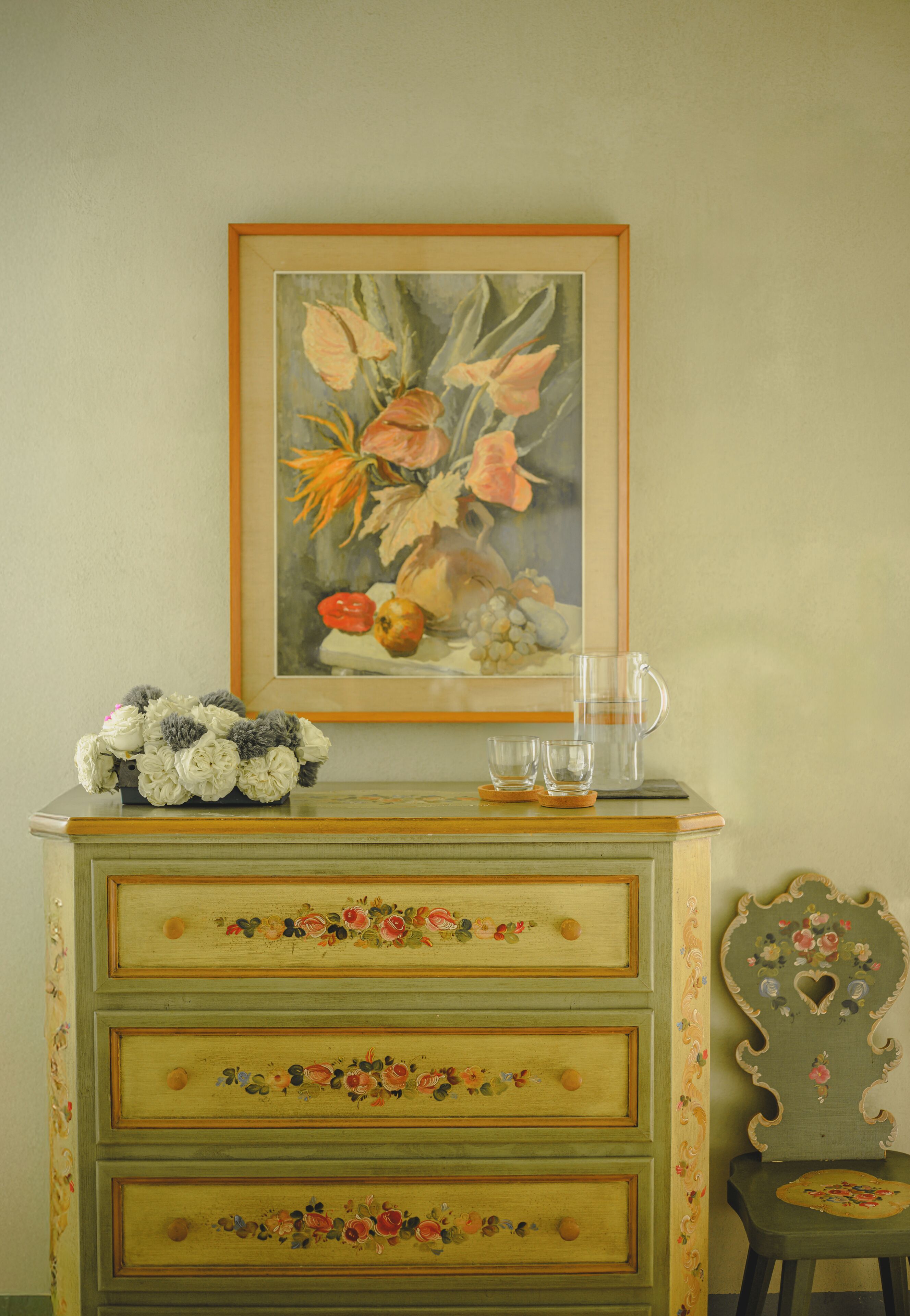 A green dresser with floral drawer knobs and a framed painting above it.