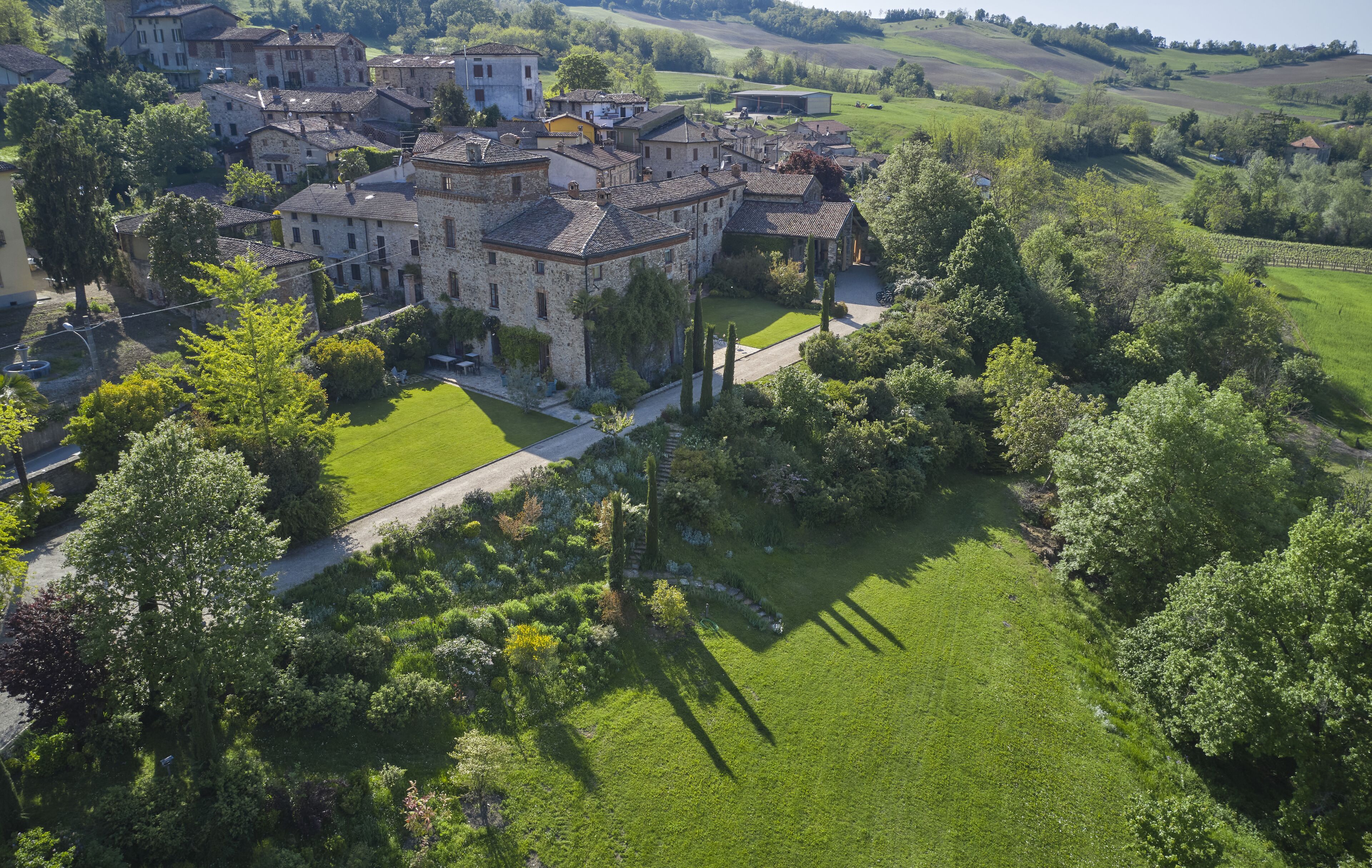 An aerial view of a historic stone building complex with multiple structures, surrounded by lush greenery and rolling hills.