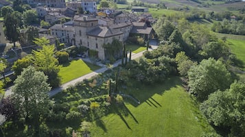 An aerial view of a historic stone building complex with multiple structures, surrounded by lush greenery and rolling hills.