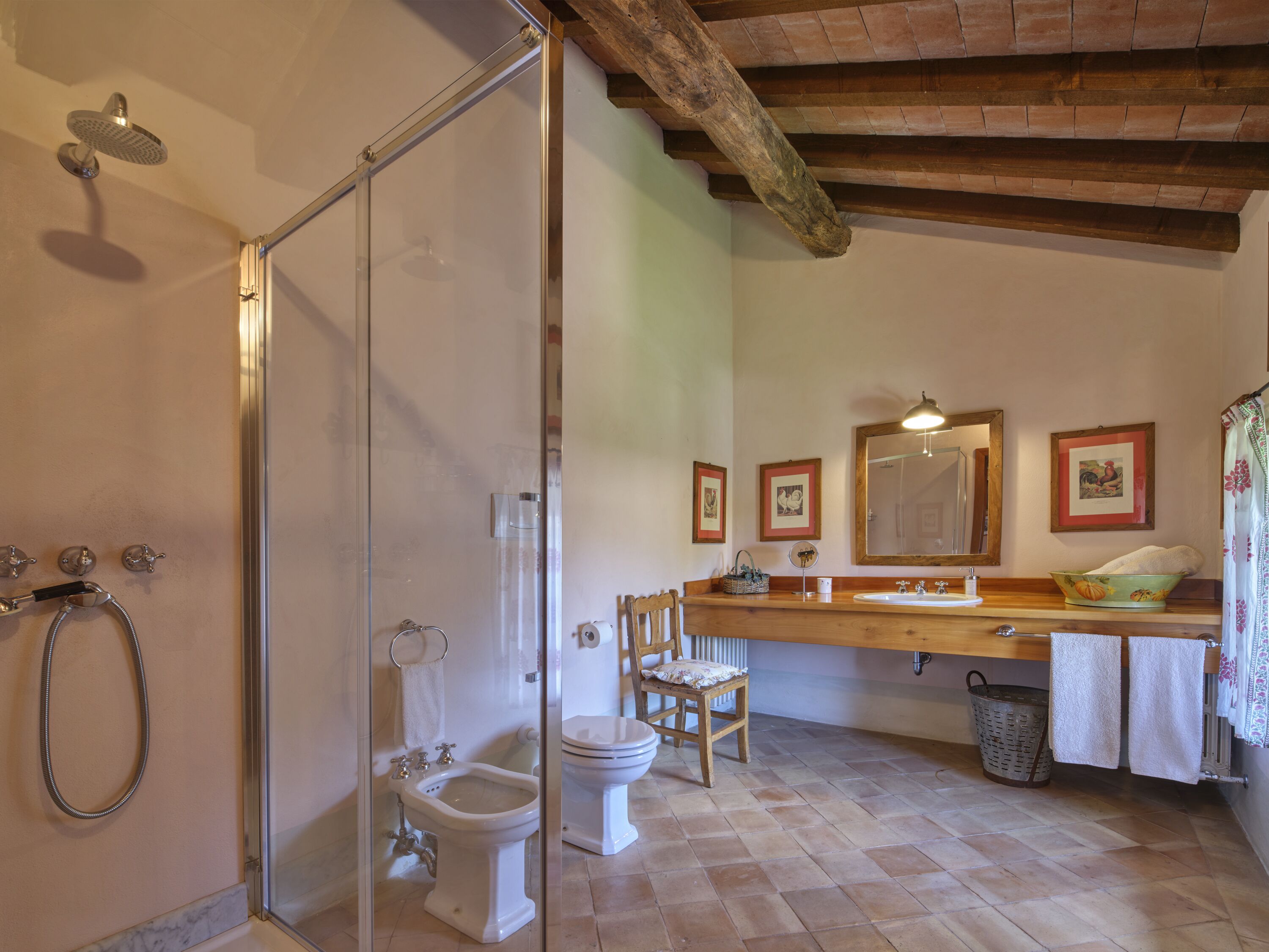 Une salle de bain avec une douche à parois de verre, des toilettes, un bidet, une chaise en bois, un lavabo avec un miroir et un radiateur.