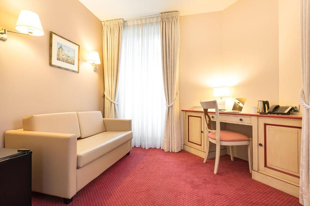 Habitación de hotel con sofá, escritorio con silla, teléfono y un cuadro en la pared.
