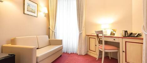 A hotel room with a sofa, a desk with a chair, a telephone, and a picture on the wall.