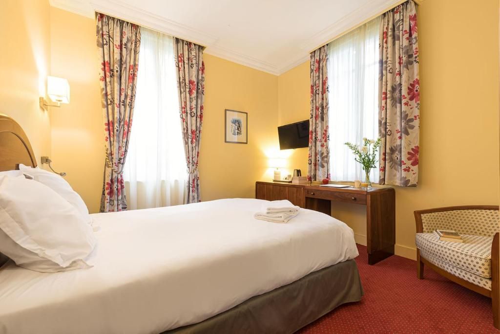 Et hotelværelse med seng, skrivebord, stol og fjernsyn.