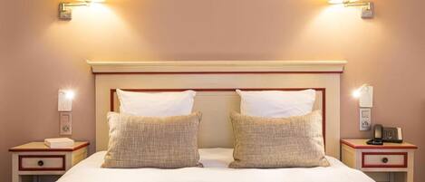Une chambre d’hôtel avec un grand lit, deux lampes de chevet, une table de chevet avec un téléphone et un luminaire fixé au mur.