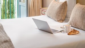 Una habitación de hotel con una cama, una computadora portátil, una taza y un croissant.