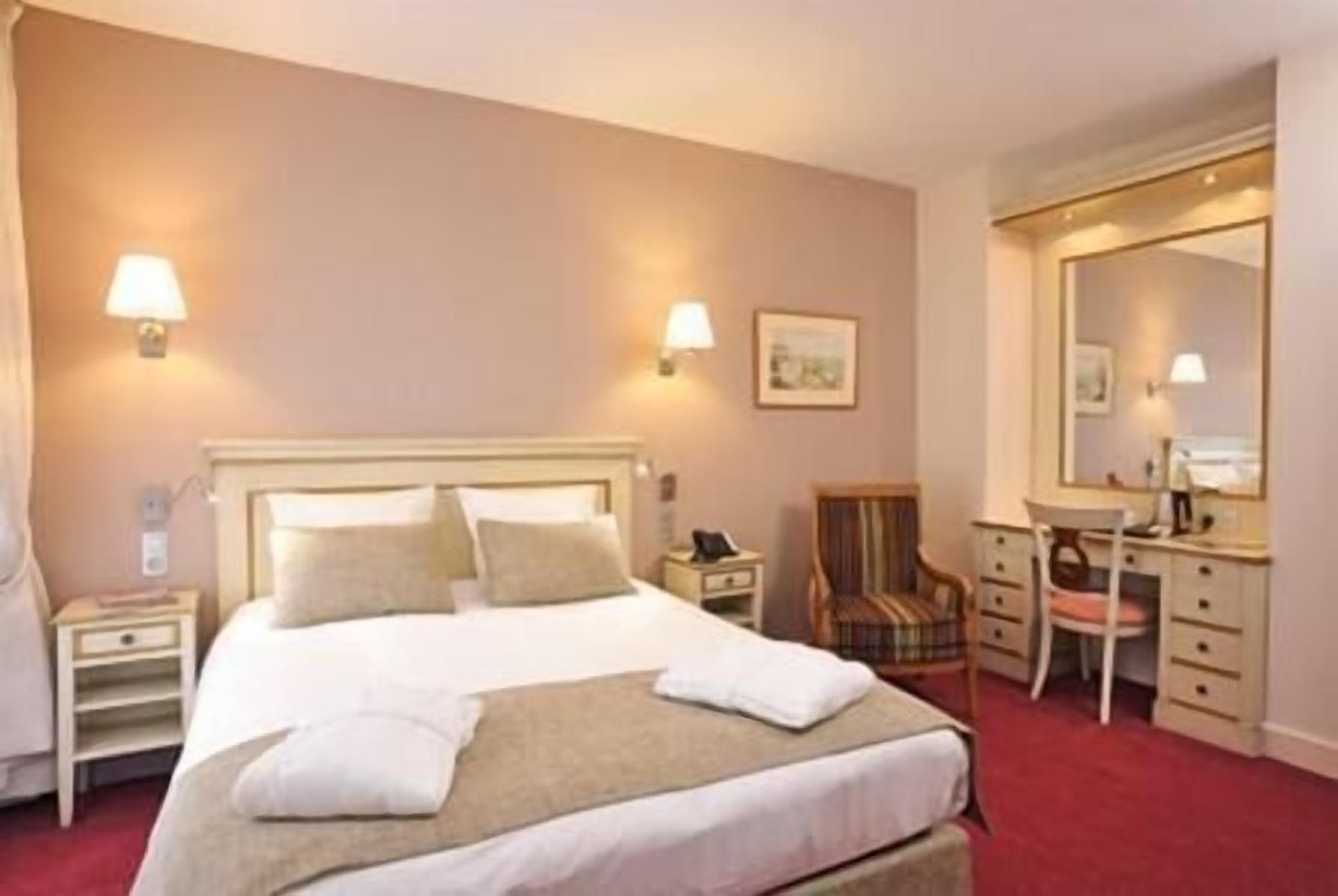 A hotel room with a bed, bedside tables, a desk, a chair, and a mirror.