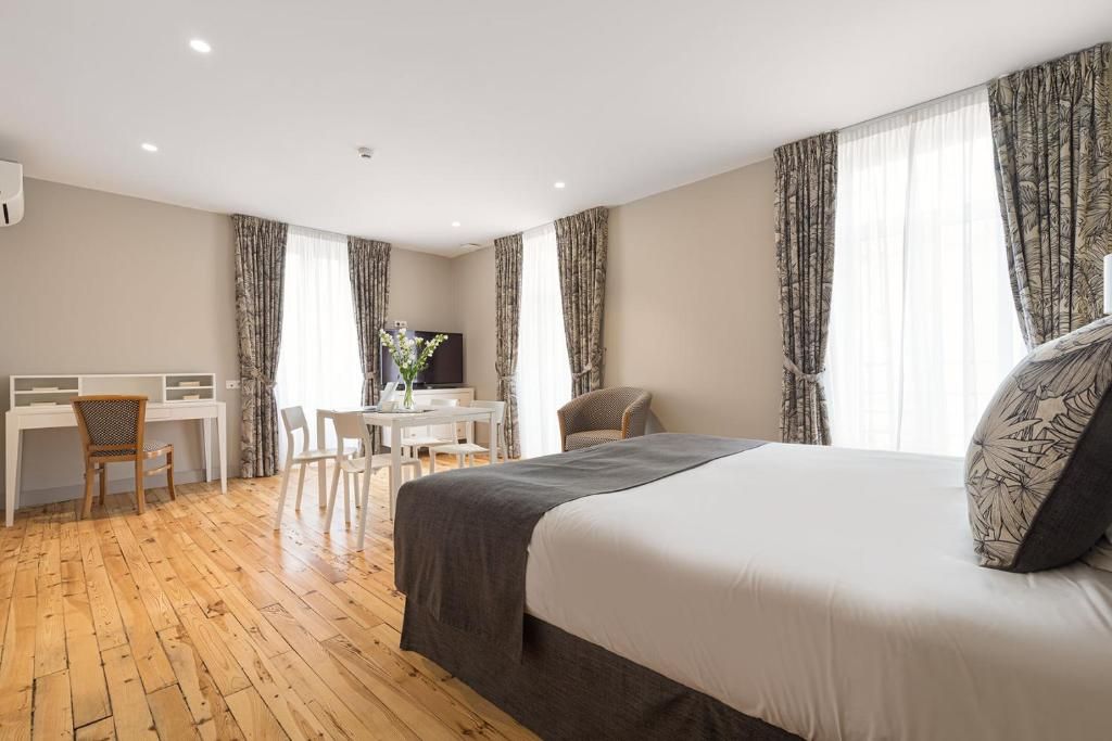 A hotel room with a bed, desk, chairs, and curtains.